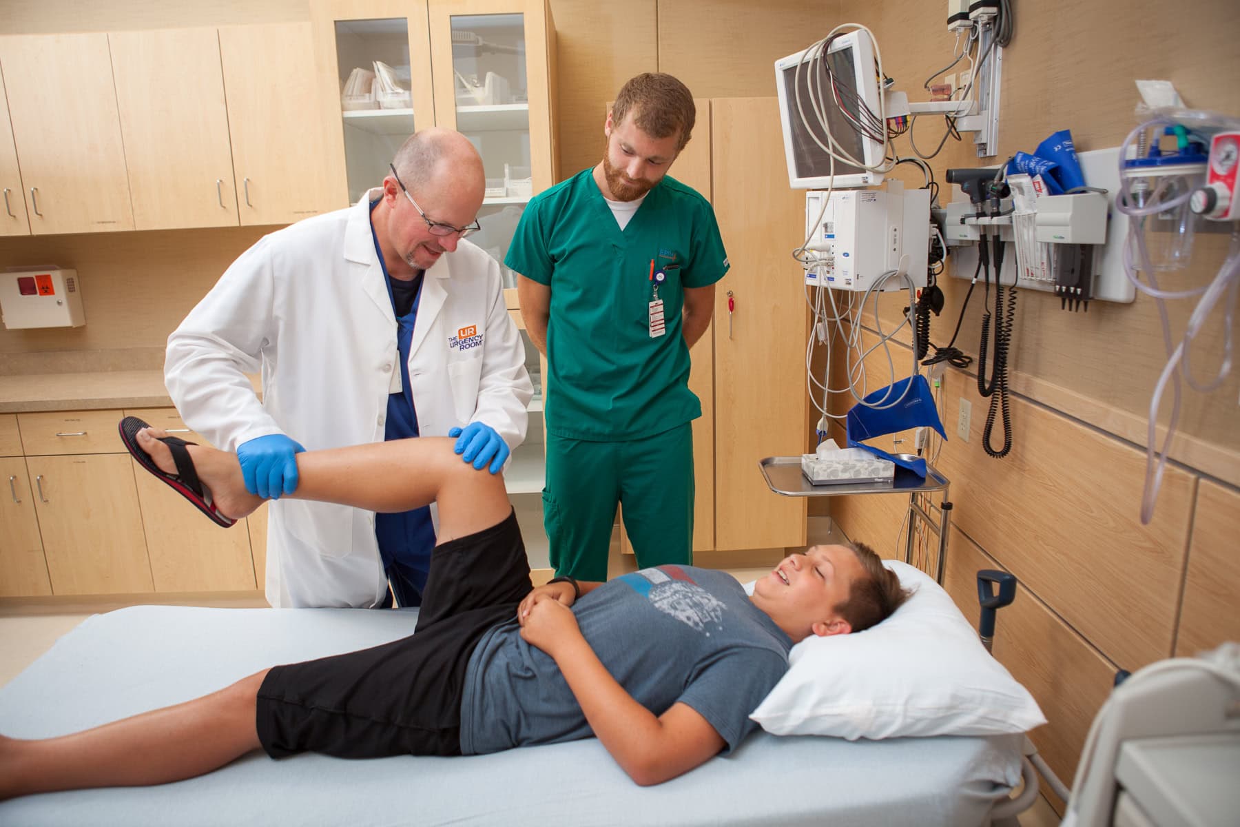 A doctor examines a patient's leg as another observes in the urgency room, where urgent care online services are also available.