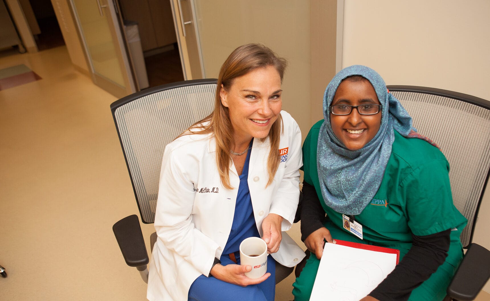 Two women, one in a white coat and one in green scrubs, smile at the camera—your friendly faces for online urgent care.