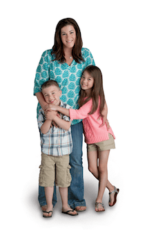 A woman stands behind a young boy and girl, smiling and hugging each other—just like family at the urgency room, safe and cared for together.